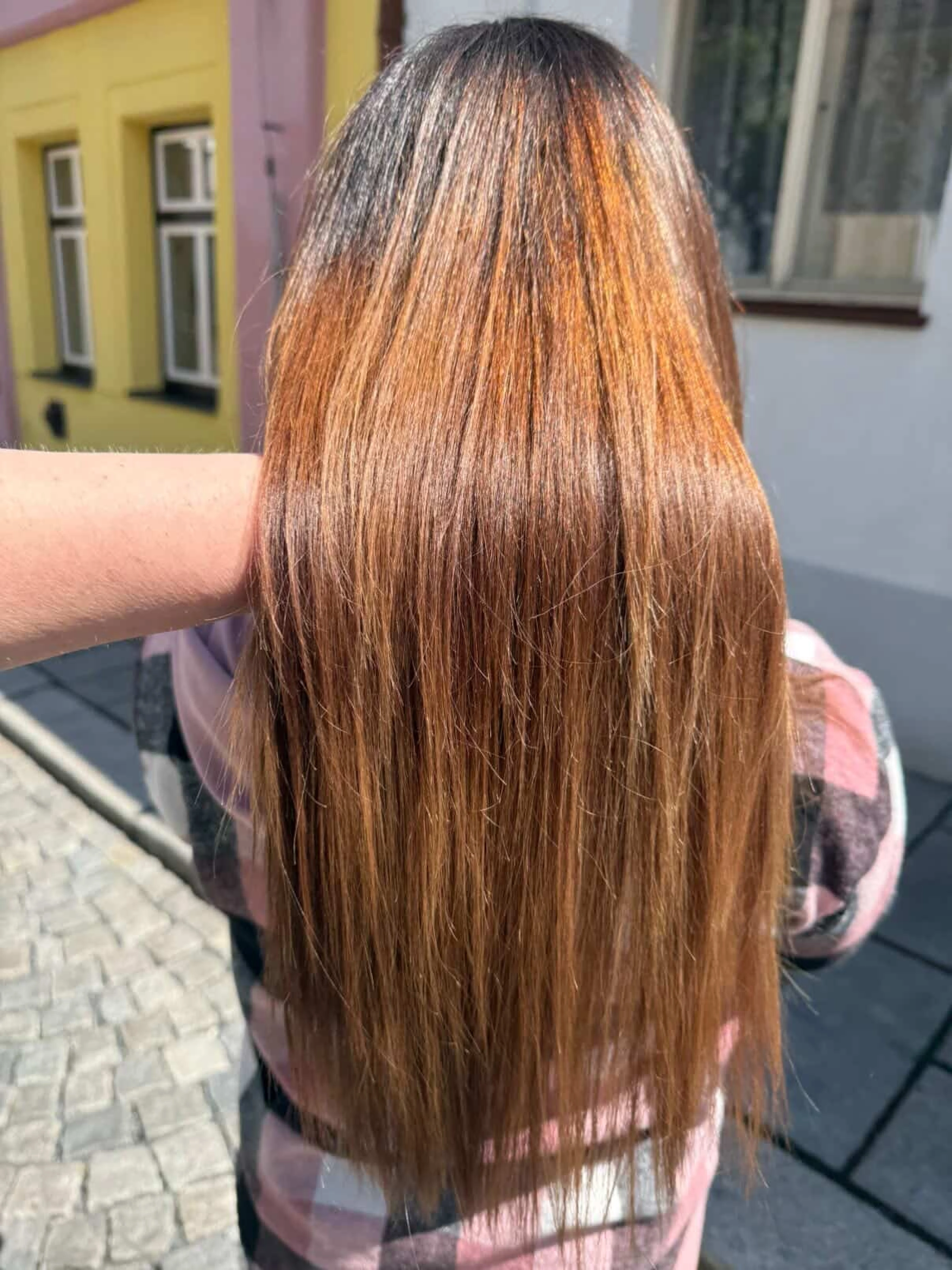Dlouhé zářivé měděně hnědé vlasy zobrazené zezadu na slunci.